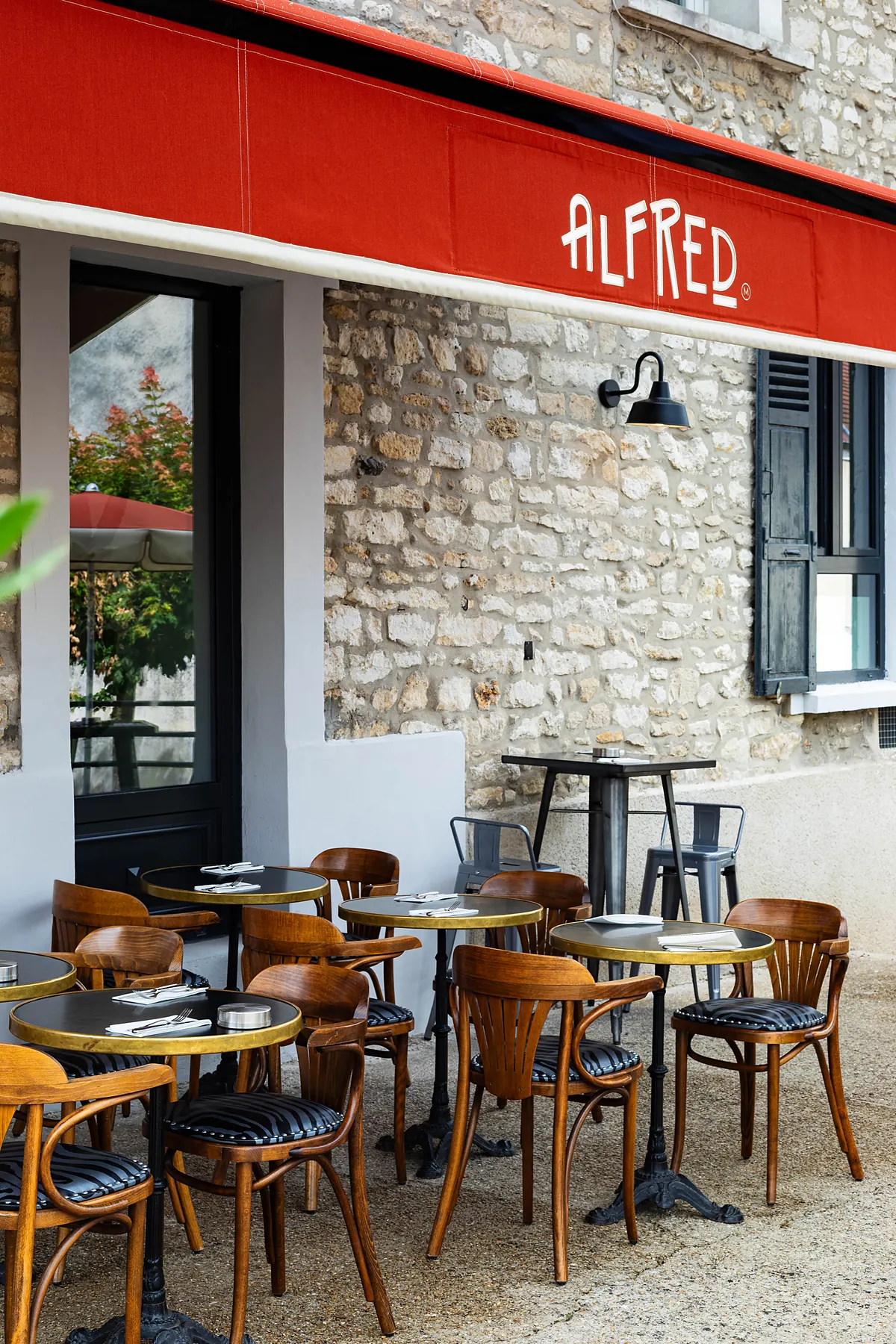 La terrasse devant la façade en pierre et l'auvent rouge Alfred
